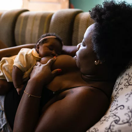 black woman laying on the couch breastfeeding her infant