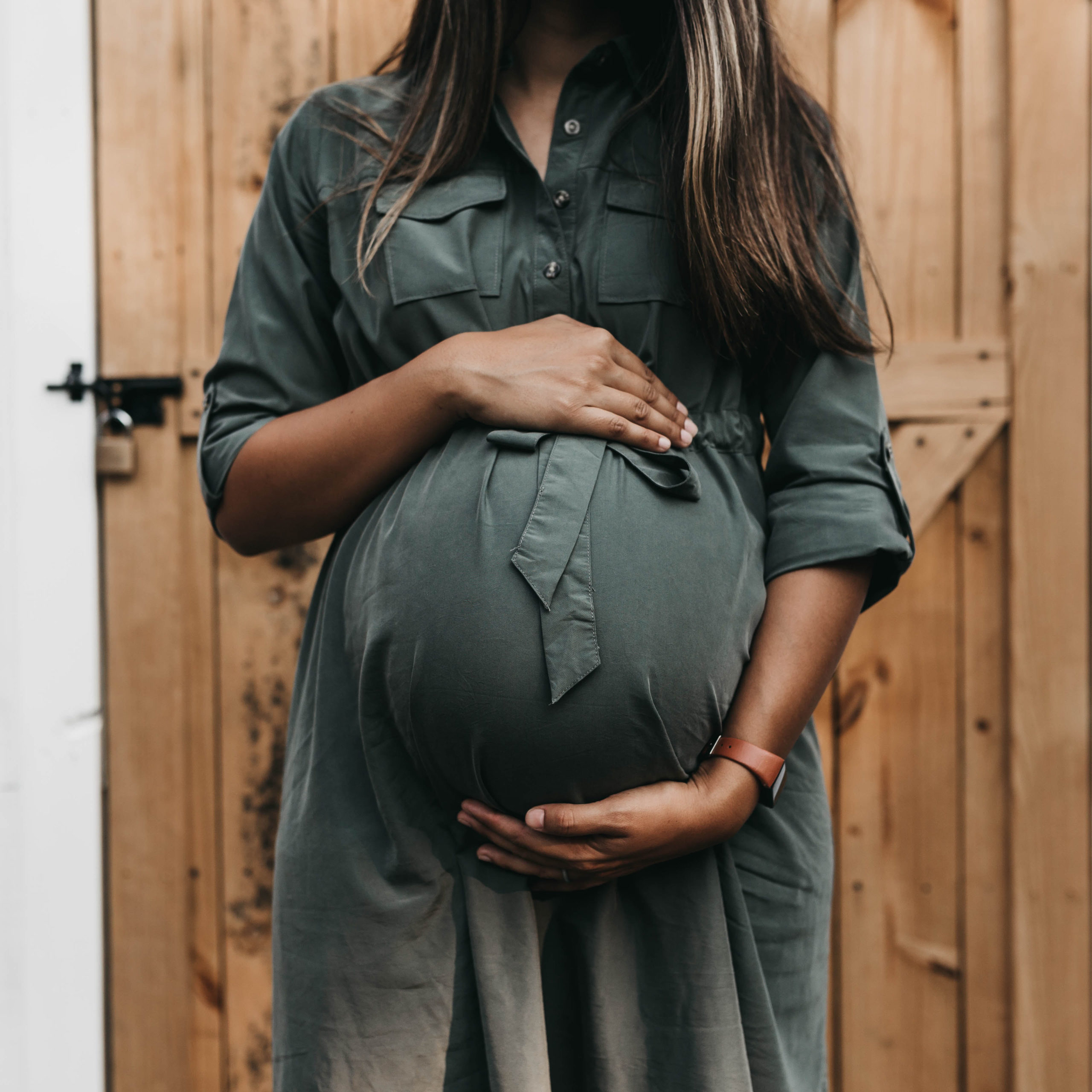 pregnant woman in green dress standing in front of a fence holding her belly