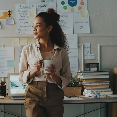 Shot of an attractive young businesswoman standing and looking contemplative while holding a cup of coffee in her home office