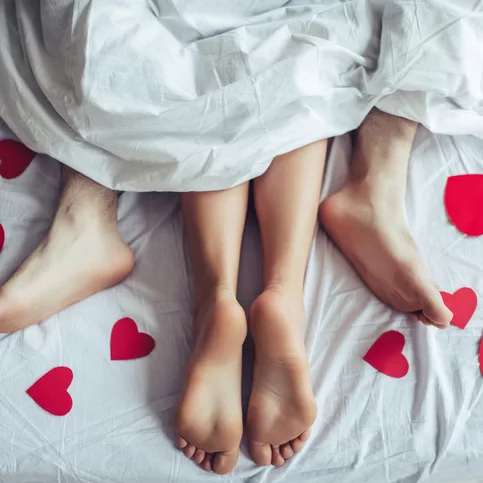 feet of two people in bed together intimately surrounded by hearts