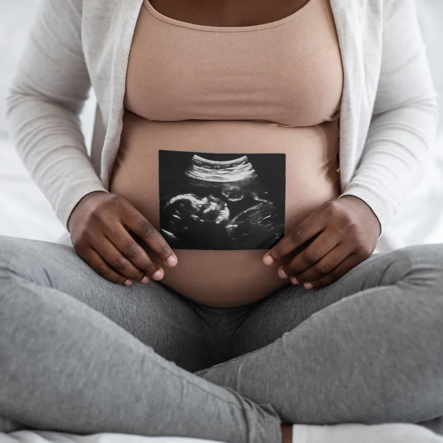 pregnant woman of color holding an ultrasound image in front of her belly